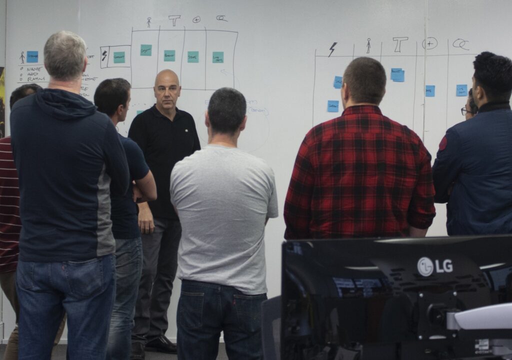 Room of people standing looking at a whiteboard